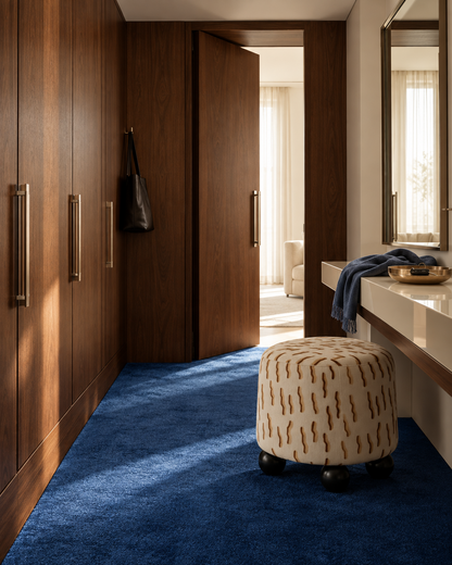 PALLINA poef met grafische bekleding en zwarte bolpoten in een hal met notenhout en een blauwe vloer